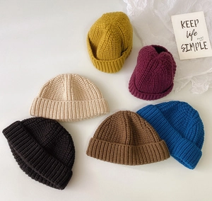 Vista plana de gorros de punto en seis colores que incluyen mostaza, burdeos, beige, negro, marrón y azul
