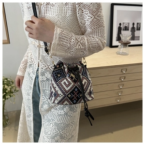 Close-up of ethnic drawstring bucket bag with colorful geometric woven patterns and leather strap