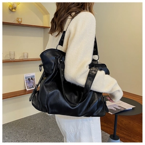 Detailed view of black textured leather tote bag with metallic buckle worn by a model