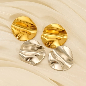 Macro detail of gold and silver irregular wavy earrings on elegant silk fabric background