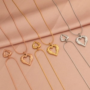 Detailed view of heart wing pendants in gold, silver and rose gold on pink silk fabric