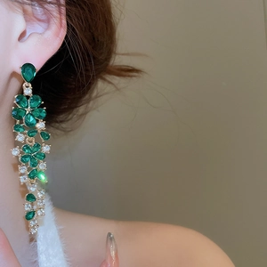 Detail of green crystal floral tassel earrings worn by model in a soft focus profile