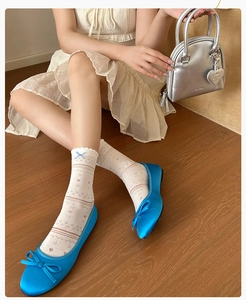 Detail of blue satin ballet flats with bow and white mesh patterned socks on wood floor