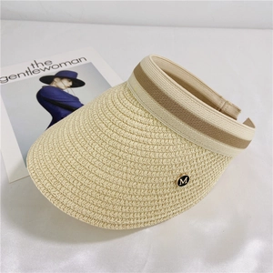 Close-up of beige straw sun visor featuring a striped elastic band and gold metal M logo