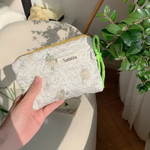 Detail of floral embroidery on cream textured lipstick bag with green braided rope