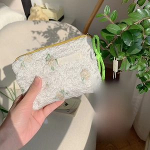 Detail of floral embroidery on cream textured lipstick bag with green braided rope