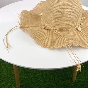Close-up of woven straw hat with scalloped brim featuring shell and rope bow details