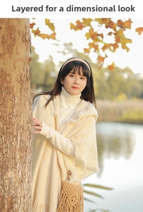 Detail of off-white knit poncho with fringe and matching sweater in an autumn park