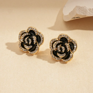 Detail of dark floral earrings with gold trim and rhinestones on textured surface
