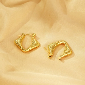 Detailed macro of gold geometric earrings with a refined hammered texture on champagne silk