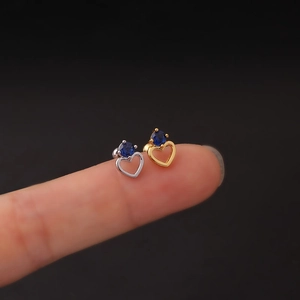 Macro shot of gold and silver heart earrings with blue zircons held on fingertips