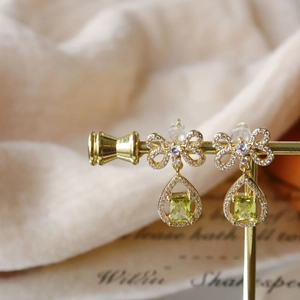 Detail of gold bow earrings with green teardrop stones on a vintage display