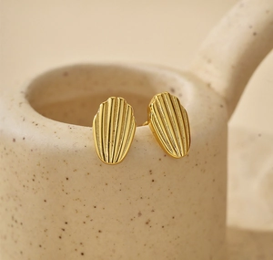 Macro shot of gold shell earrings with vertical stripes on a beige ceramic cup