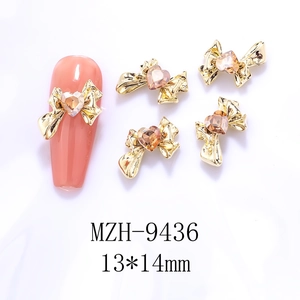 Golden 3D hollow bow nail art charms with heart gemstone detail on orange nail tip