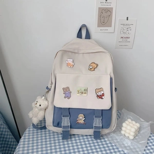 Detail of cream and blue canvas backpack featuring cute bear charms on a checkered table