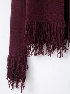 Detail view of burgundy knit cardigan featuring thick fringe tassels on hem and cuffs