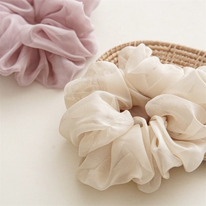 Close-up of pink and beige chiffon scrunchies with soft pleated texture on woven mat