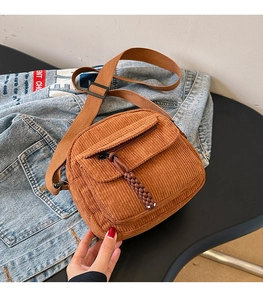 Detailed texture of brown corduroy crossbody bag with zipper pocket on denim background