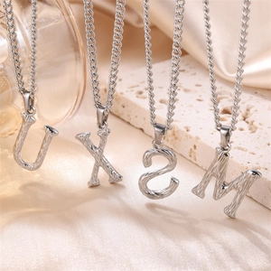 Close-up of textured silver initial pendants with curb chain on a minimalist display