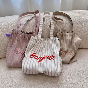 Detailed close-up of three striped canvas tote bags with Bonjour embroidery and drawstring