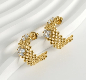 Détail de boucles d'oreilles dorées en C avec texture perlée et deux zircons carrés