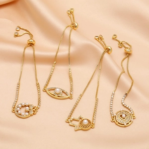 Detalle de cuatro pulseras doradas con dijes de ojo, corazón y perlas sobre satén champán