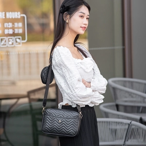 Detail of black V-quilted crossbody bag with mini round pouch on adjustable strap