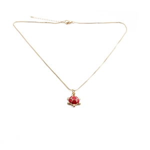Detail view of a gold-plated necklace featuring a vibrant red enamel turtle pendant