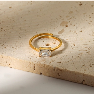 Close-up of golden irregular ring with emerald cut zircon on beige stone base