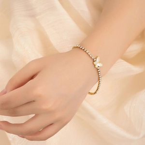 Detailed shot of a gold tennis bracelet featuring white crystals and a pearl butterfly charm