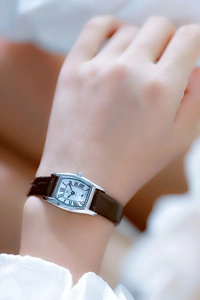 Detail of a rectangular silver quartz watch with a brown leather strap on a model wrist