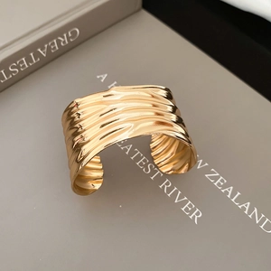 Detail view of the wide gold pleated metal cuff bracelet with wavy textured finish
