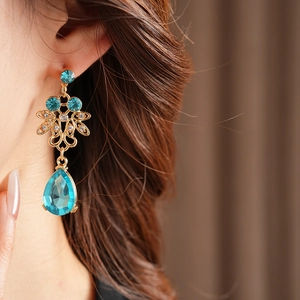 Close-up of vintage gold earrings with blue teardrop crystals worn by a model