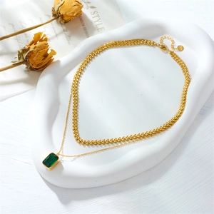 Double-layered gold titanium necklace with emerald square gemstone pendant on white tray