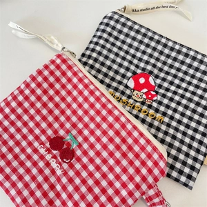 Detail of embroidered plaid pouches featuring cherry and mushroom motifs with zipper straps