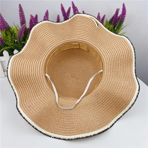 Detail of wavy brim straw sun hat with black and white stitching and white chin strap
