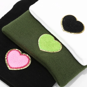 Close-up of knit beanies with plush heart patches featuring golden sequin trim and texture