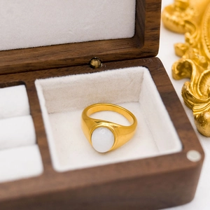 Golden signet ring with white agate gemstone displayed in a walnut wood jewelry box