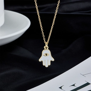 Gold Hamsa Hand necklace with white enamel Evil Eye pendant on black velvet background