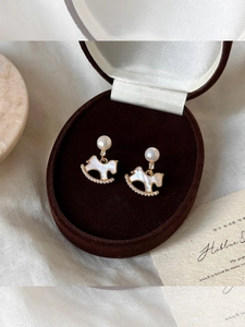 Close-up of gold plated rocking horse earrings with pearls on a silk background