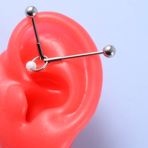 Detail of industrial barbell earring with opal ring on a realistic red ear model