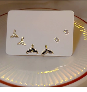 Detail view of gold whale tail earrings and zircon studs set on a display card