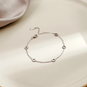 Close-up of silver geometric heart charm bracelet on a ceramic tray with soft shadows