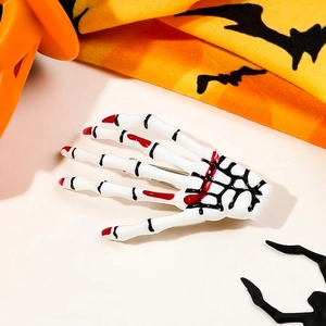 Close-up of Halloween skeleton hand hair clip with red accents on a pumpkin background