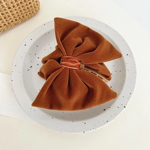 Detail of a large caramel brown velvet bow hair clip on a minimalist ceramic plate