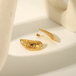 Gros plan détaillé de boucles d'oreilles dorées à texture coquillage sur bloc blanc minimaliste