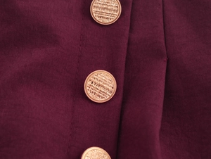 Close-up of golden embossed buttons and woven burgundy fabric on straight trousers