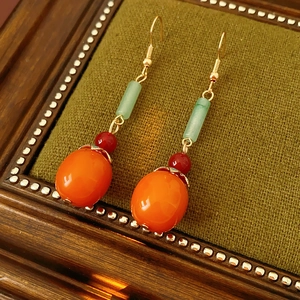 Detailed close-up of retro persimmon drop earrings with orange and jade beads on velvet