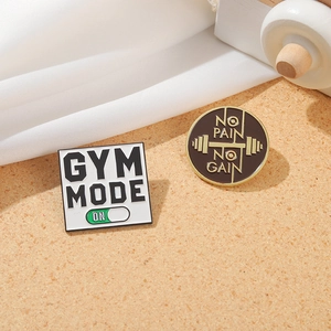 Detail view of Gym Mode and No Pain No Gain enamel pins on textured background