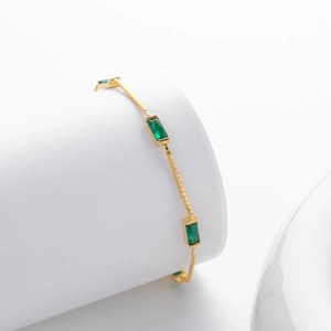 Detailed shot of a gold square link bracelet with three bezel-set green rectangular gems